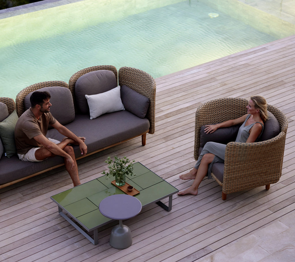 Twee mensen zitten in comfortabele lounge stoelen rondom een stijlvol salontafel, met een sereen waterobject op de achtergrond.