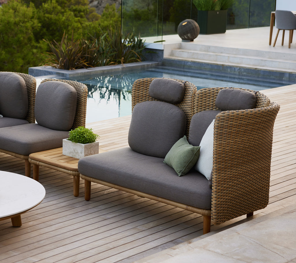 Stijlvolle sofa met hoge rugleuning en gebogen armleuningen, met grijze kussens en een mix van decoratieve kussens op een houten dek.