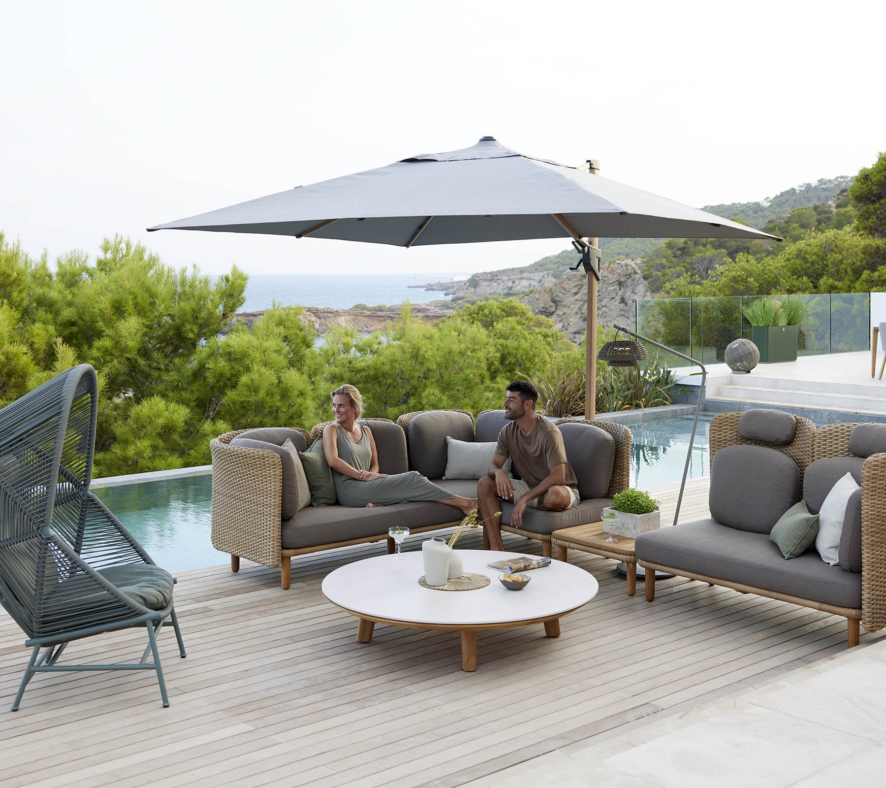 Een stijlvolle loungehoek met comfortabele zitplaatsen, een grote parasol en een ronde tafel, omringd door greenery en een vredig uitzicht.