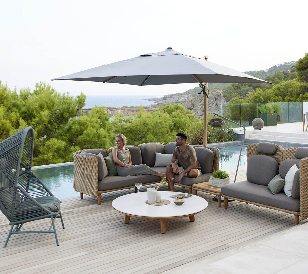 Een stijlvolle loungehoek met comfortabele zitplaatsen, een grote parasol en een ronde tafel, omringd door greenery en een vredig uitzicht.