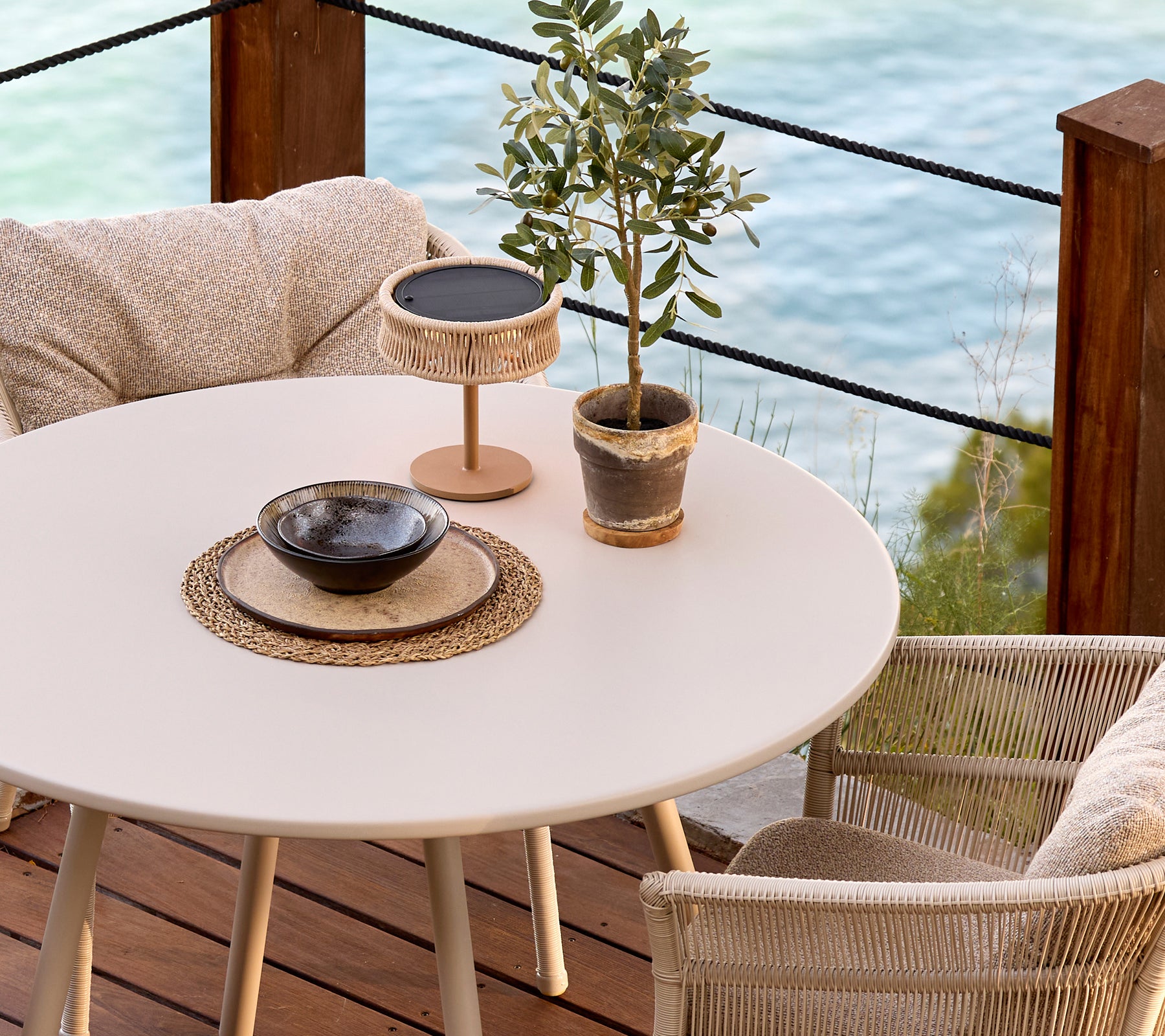 Wit rond tafel met gevlochten stoelen, decoratieve plant en een zwarte kom in een moderne lounge-instelling.
