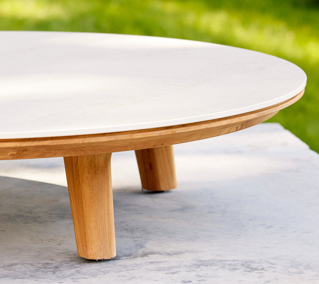 Close-up van een ronde salontafel met een glad oppervlak en houten poten, die het elegante ontwerp en vakmanschap benadrukt.