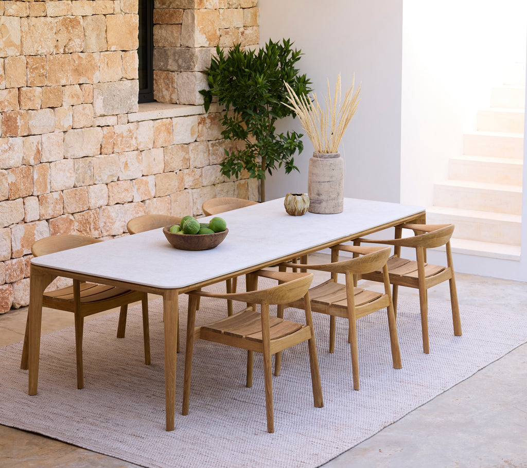 Moderne eetopstelling met een witte tafel en houten stoelen tegen een stenen muur.