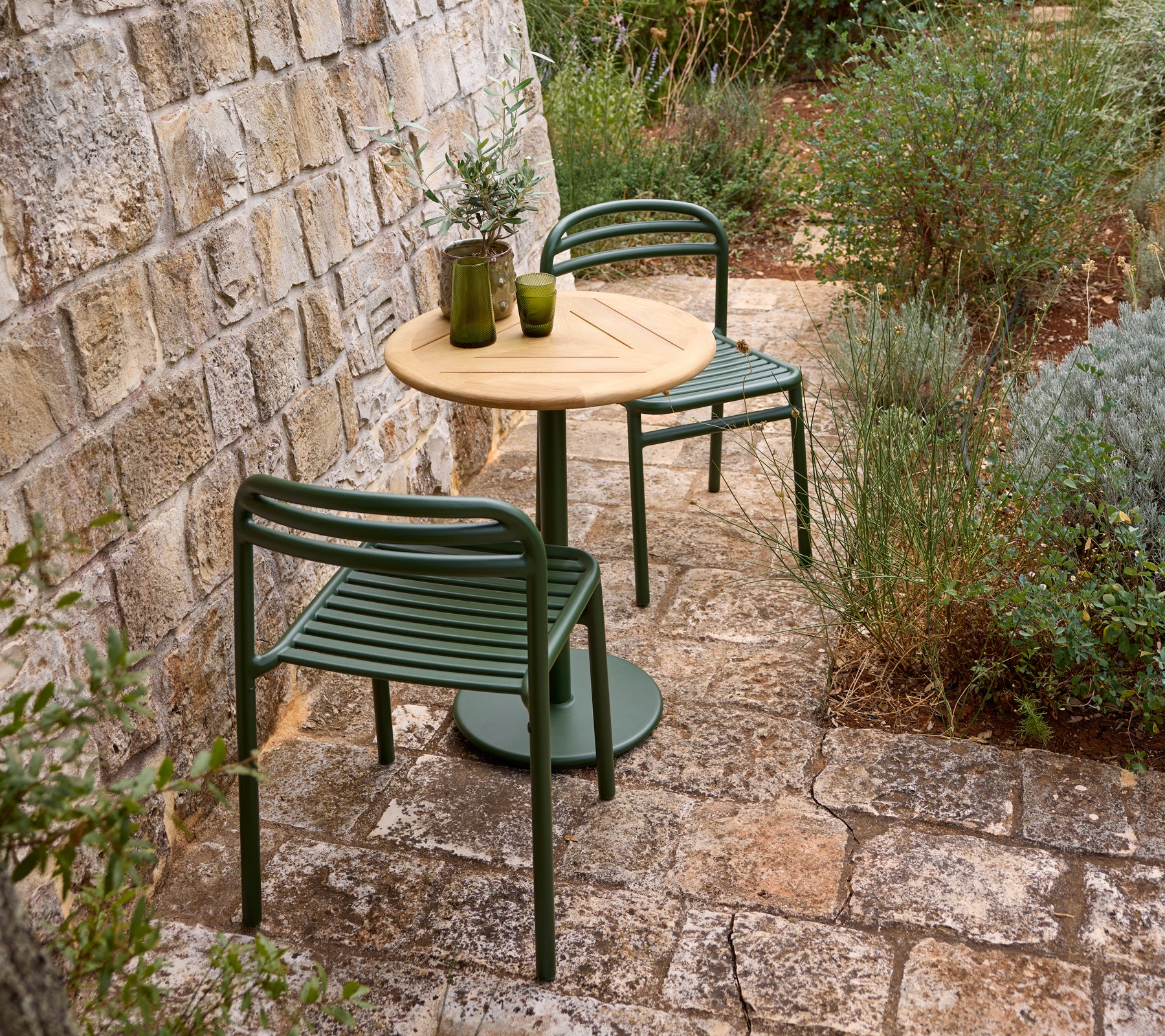 Buitensetting met een groene stoel, houten tafel en glazen vaas.