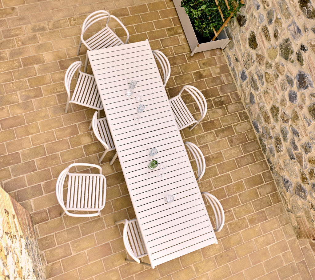 Luchtfoto van een zandkleurige buitentafel met acht Bliss-stoelen, geplaatst op een stenen terras.