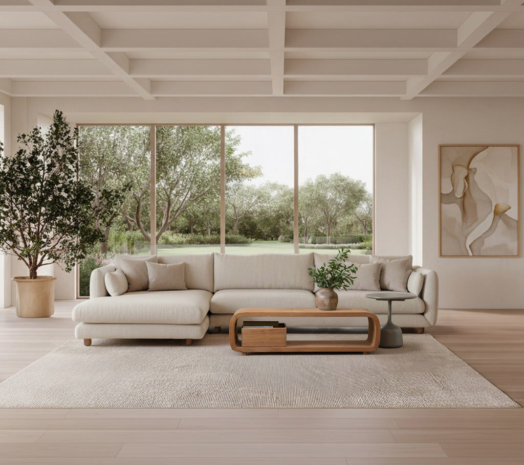 Lichtgrijze bank met houten salontafel en grote plant in een moderne lounge-setting.