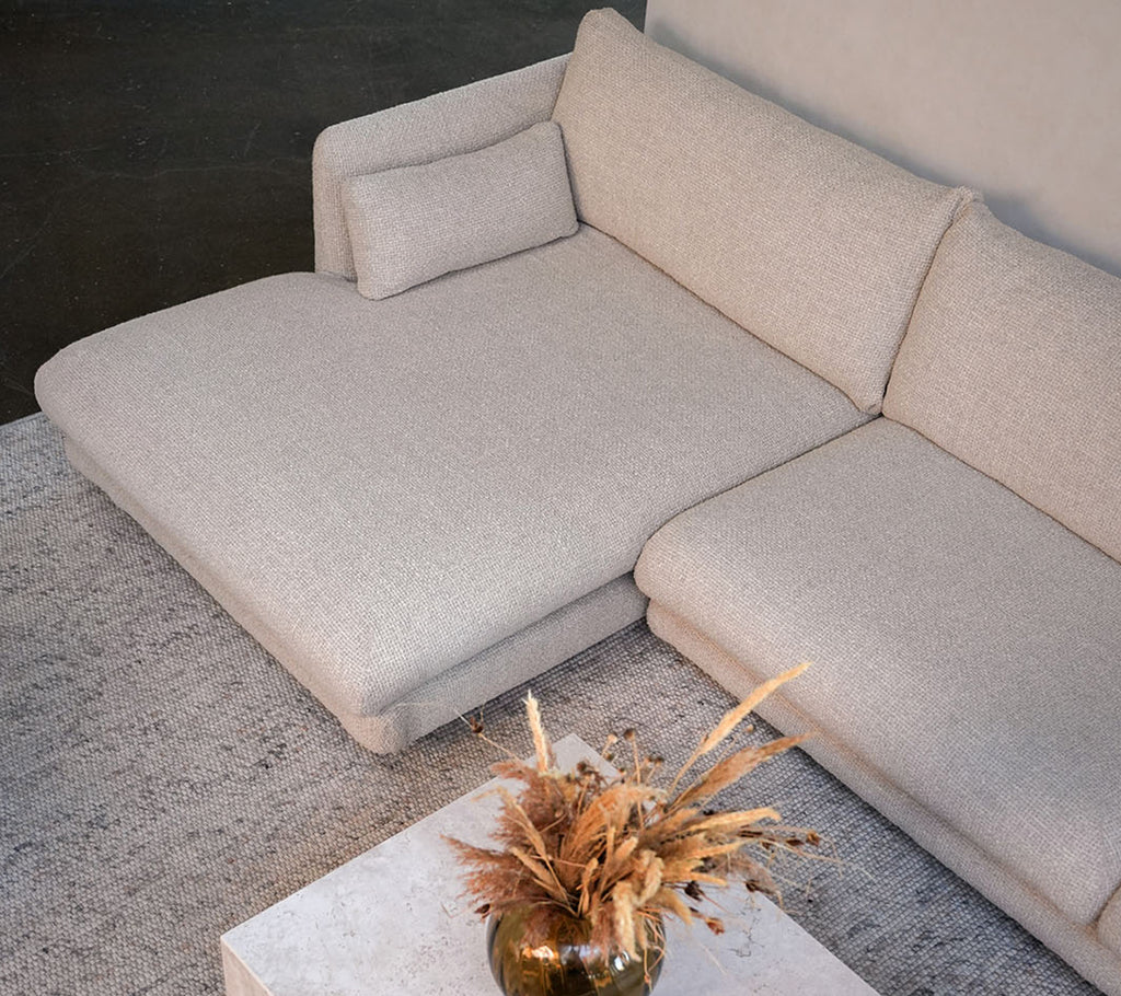 Moderne beige bank met een witte tafel en een decoratieve vaas in een stijlvolle lounge-setting.