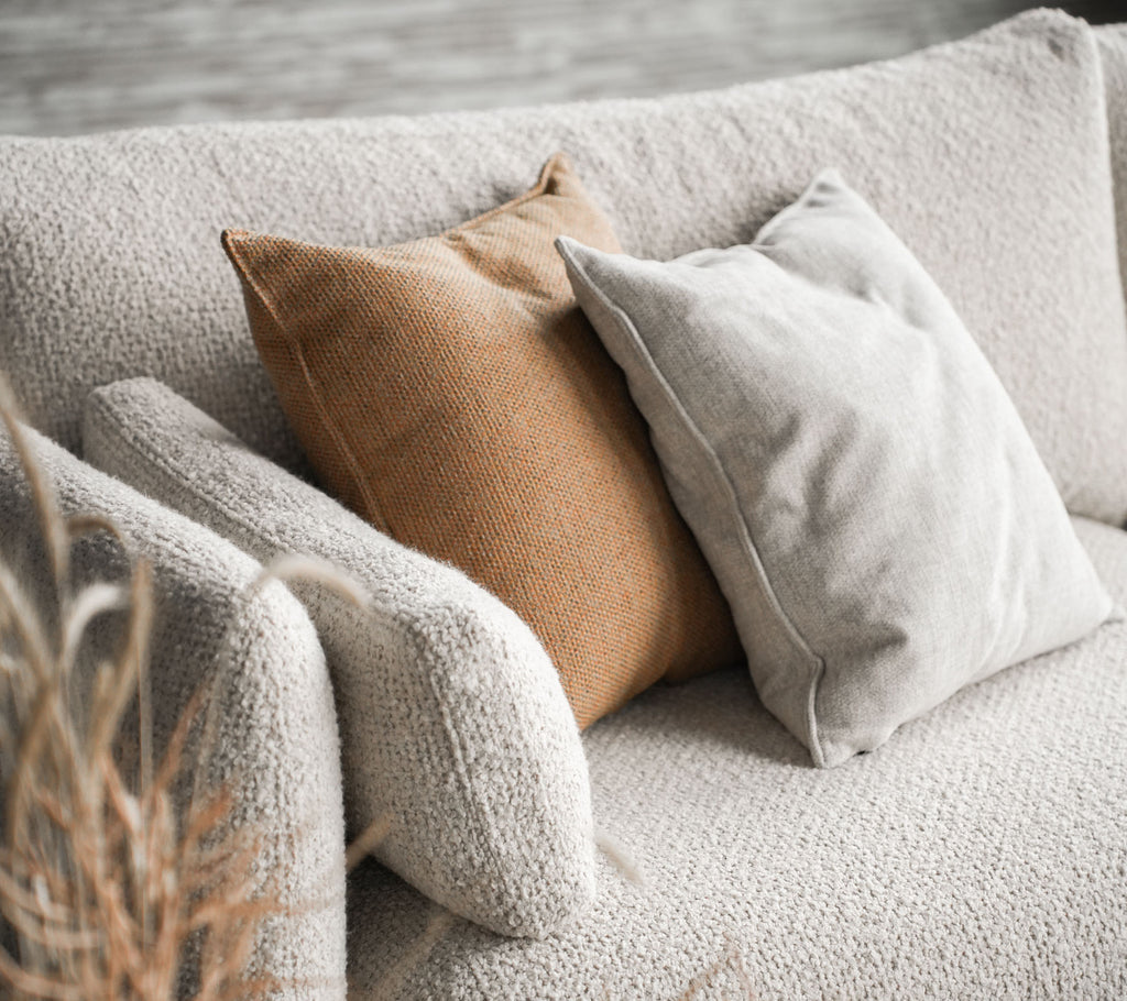 Gezellige bank met Bloom in zandkleur met twee kussens, een in beige en de andere in warm bruin, wat een stijlvolle touch toevoegt.