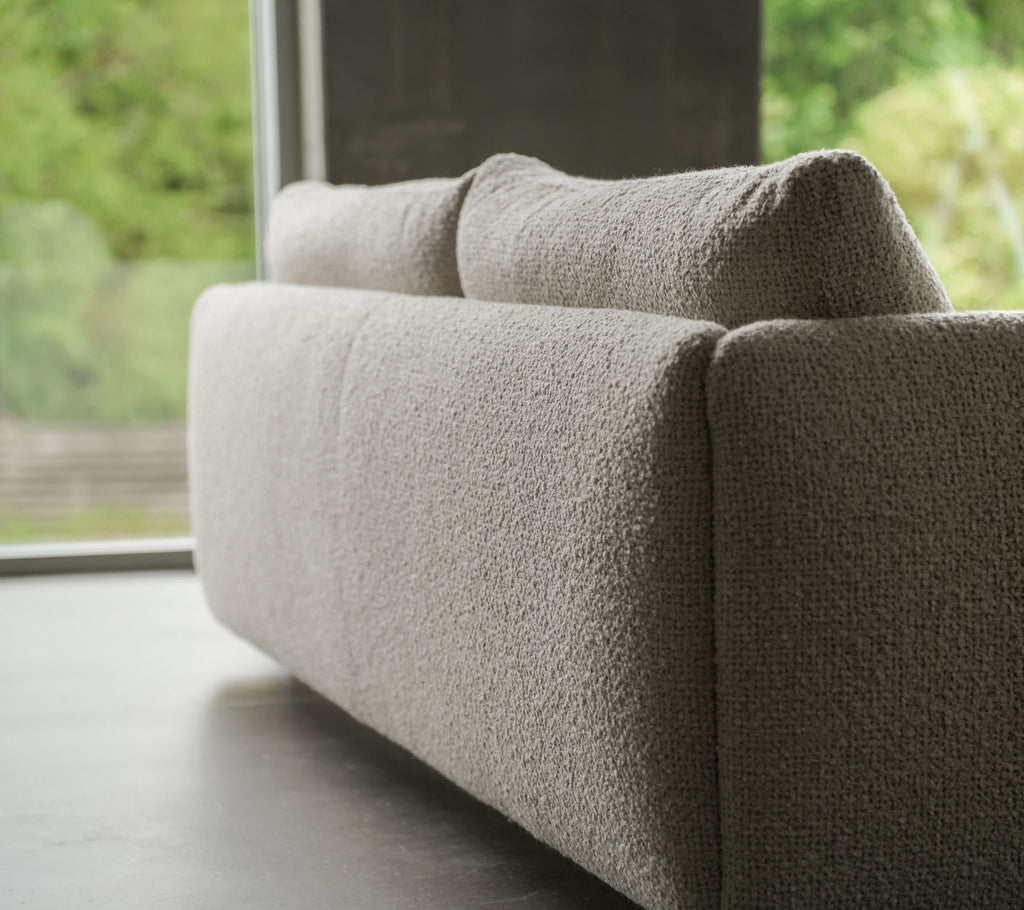 Moderne bank met een gestructureerde zandkleurige stof, benadrukt door elegante teakpoten, die de flair van Cane-line en zachte kussens toont.
