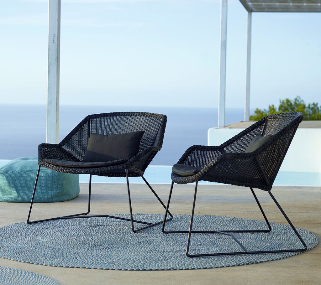 Twee moderne zwarte stoelen met een blauwe kussen op een rond tapijt bij het zwembad.