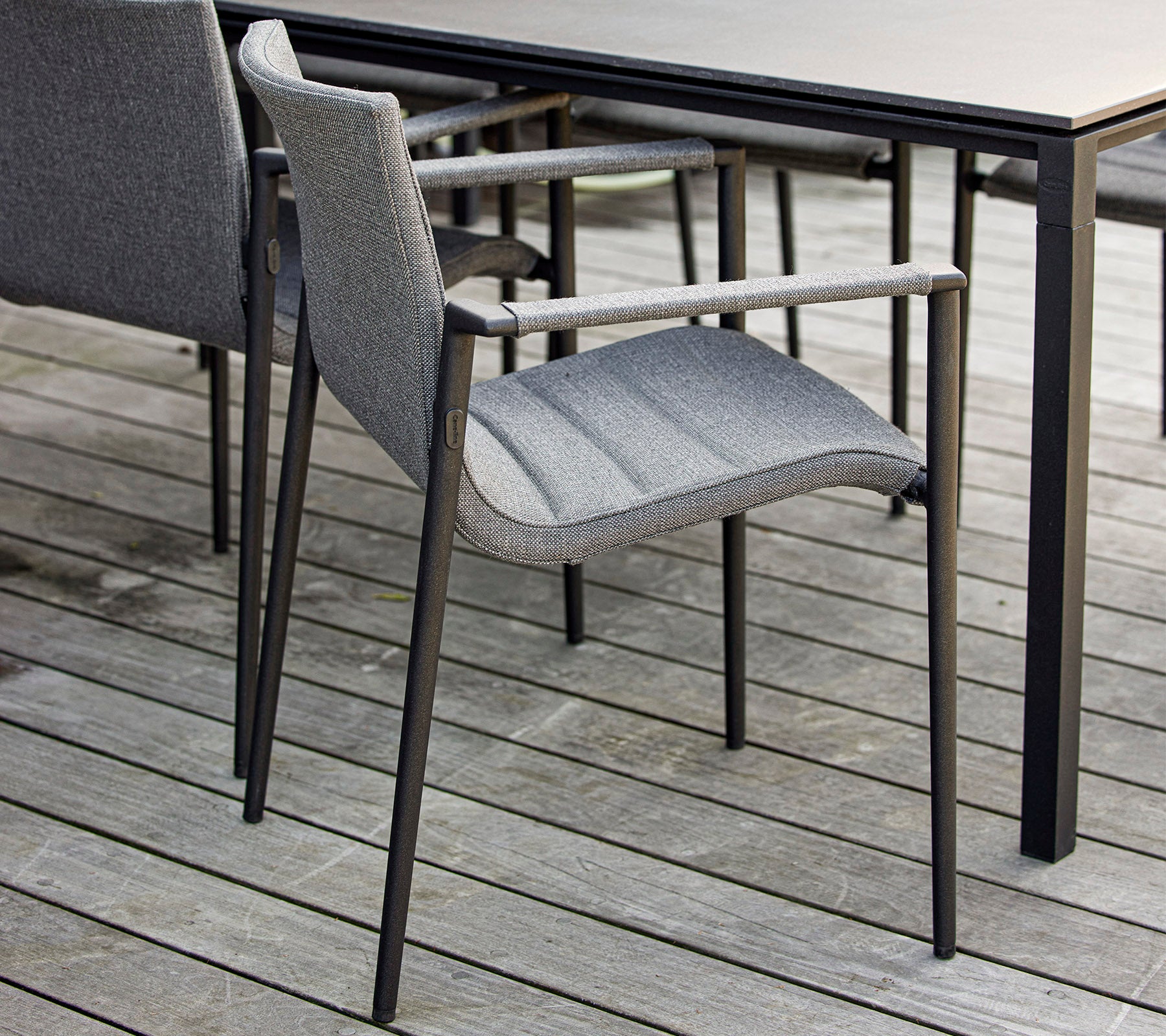 Stijlvolle grijze stoel met armleunen, geplaatst naast een elegant zwarte tafel op een houten oppervlak. Ideaal voor moderne buitenomgevingen.