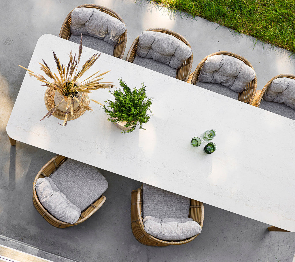 Een lange, elegante tafel omringd door stijlvolle stoelen, versierd met een decoratieve plant en glazen flessen bovenop.