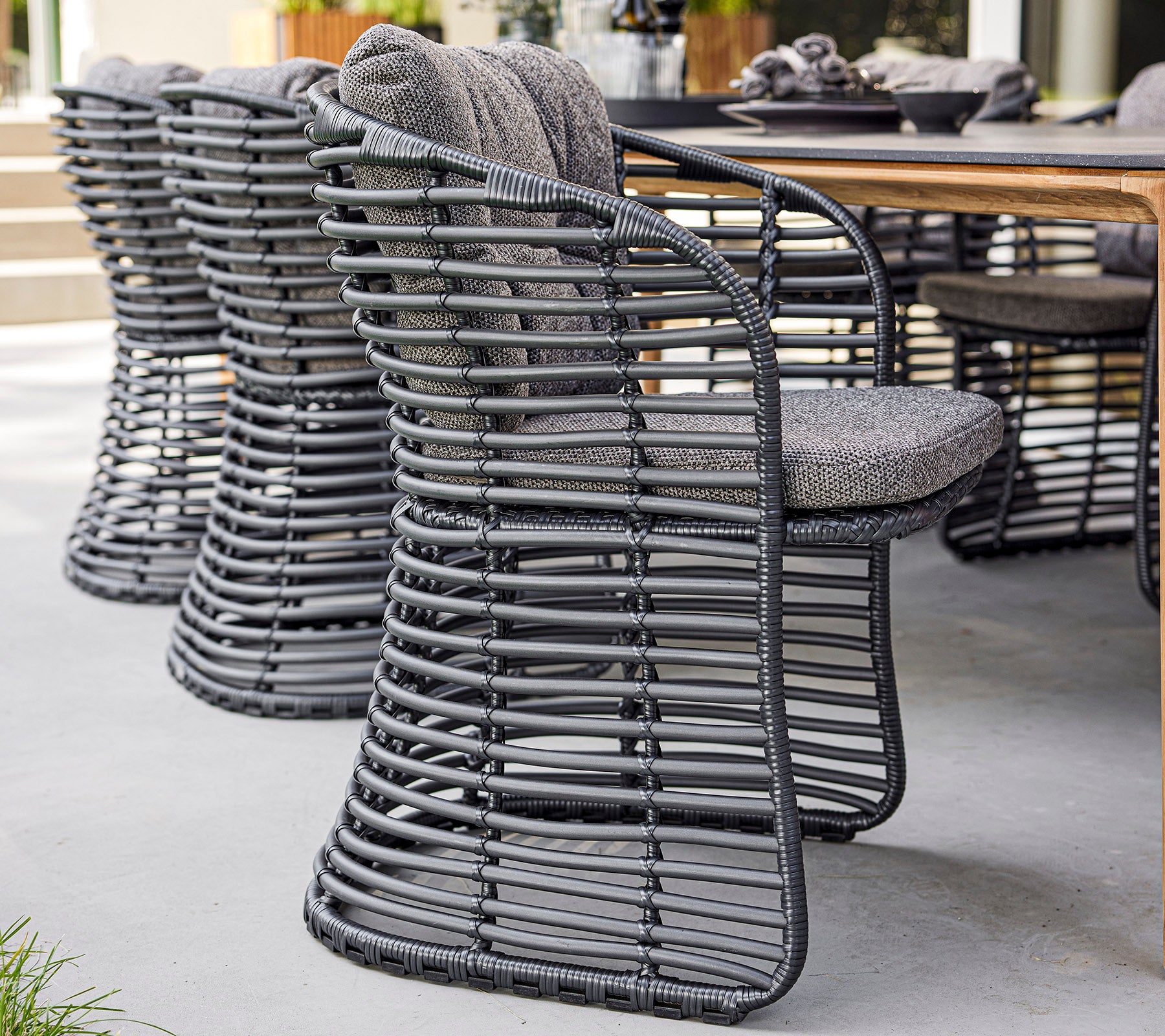 Stijlvolle gevlochten stoelen met een modern ontwerp en gevoerde zitplaatsen, naast een houten tafel geplaatst.