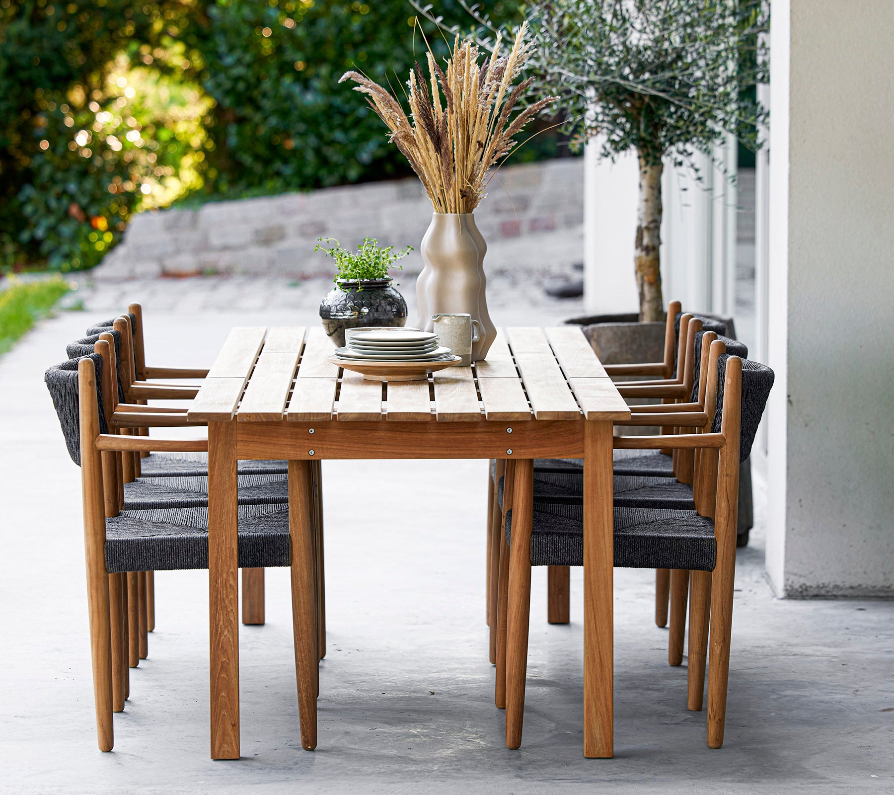 Een houten tafel omringd door acht stijlvolle stoelen, versierd met een vaas en groen, wat een uitnodigende eetruimte creëert.