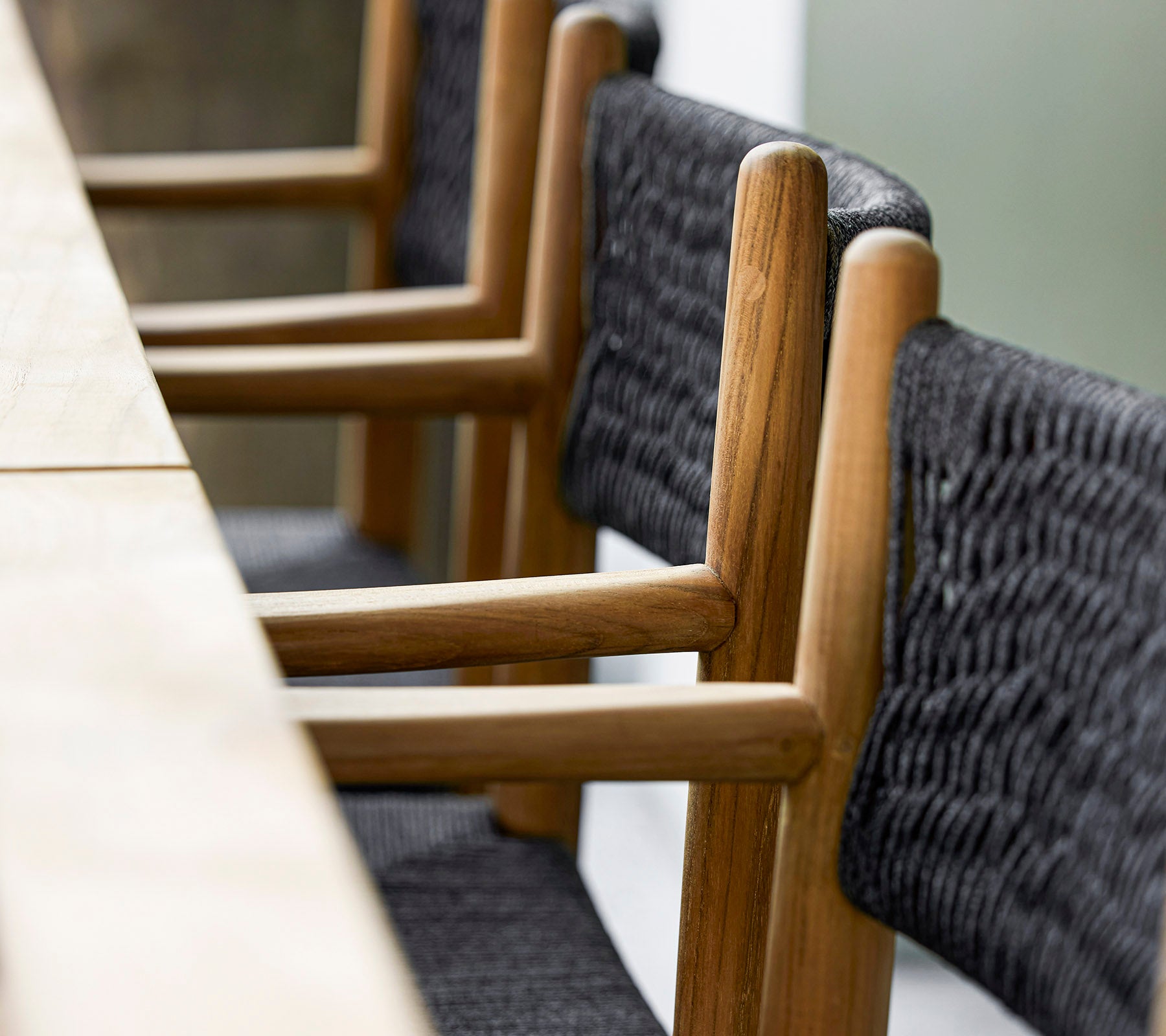 Een close-up van moderne houten stoelen met geweven zwarte textieldetails, netjes geplaatst naast een lange houten tafel.