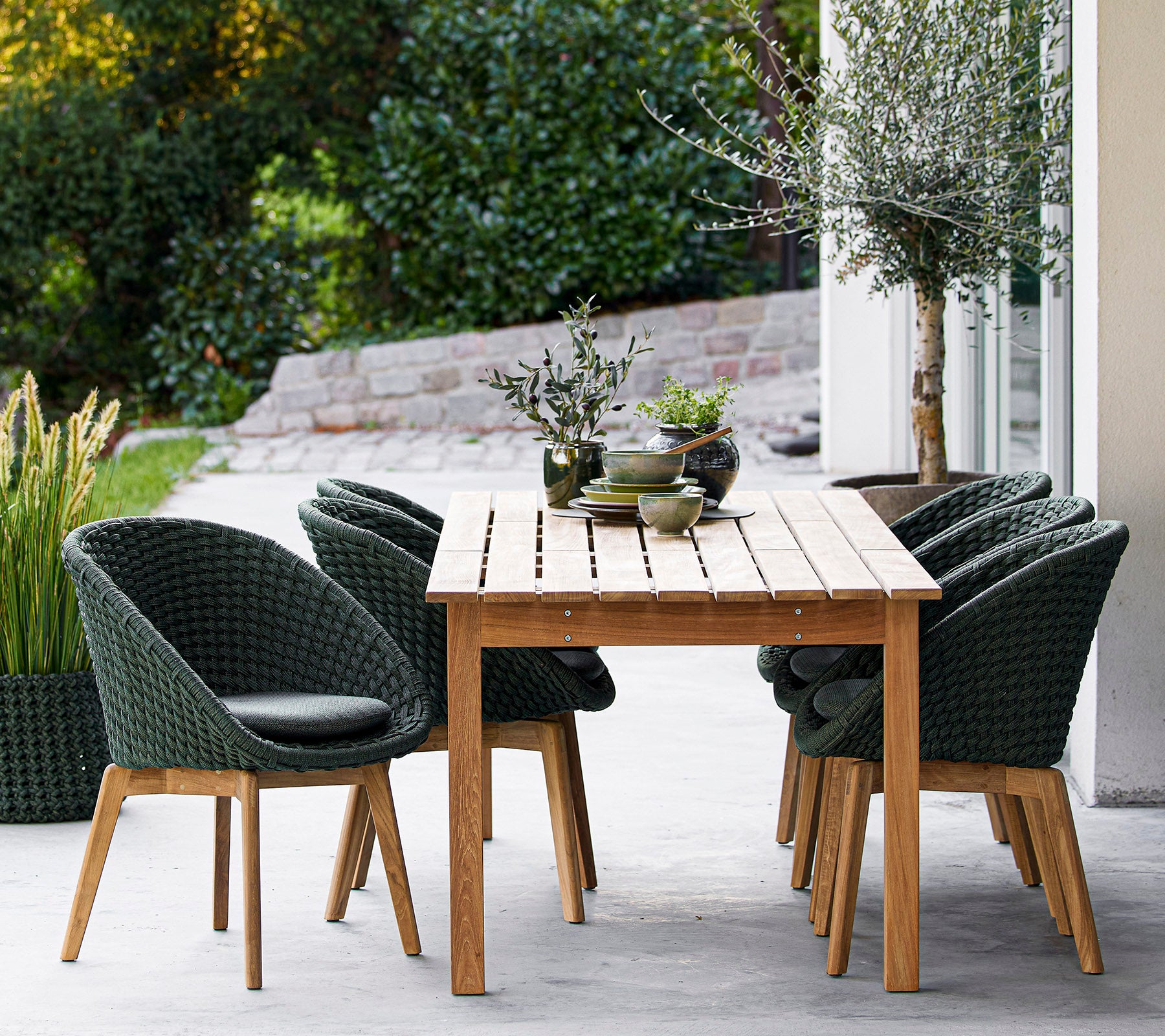 Een houten tafel omringd door stijlvolle groene stoelen, met decoratieve planten en een serene achtergrond. Ideaal voor dineren of ontspanning.