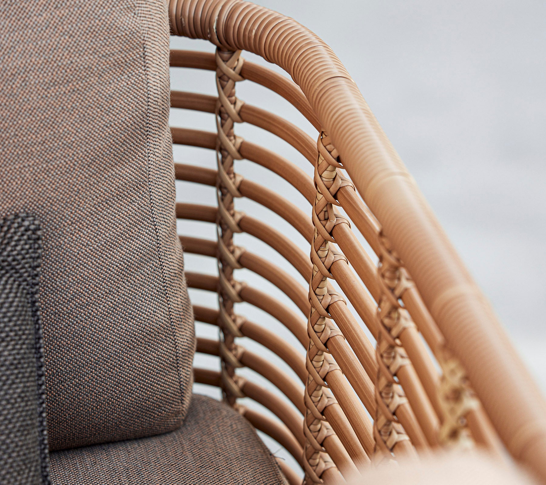 Close-up van een stijlvolle fauteuil met gevlochten rattan-details en zachte kussens in neutrale tinten, die modern design laat zien.