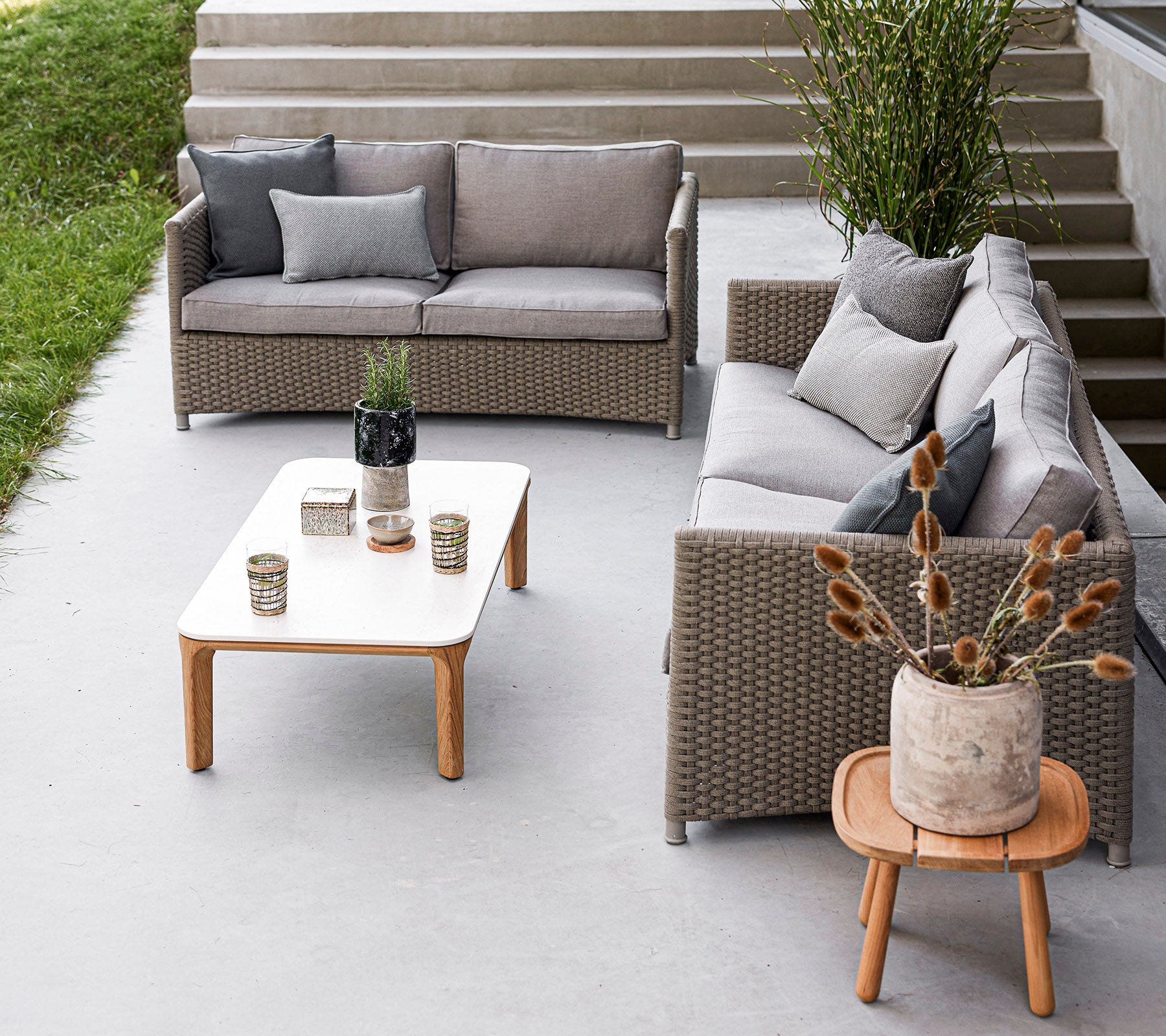 Stijlvolle buitensitgelegenheid met een grijze bankset, een houten tafel, decoratieve vazen en potplanten. Ideaal om te ontspannen.