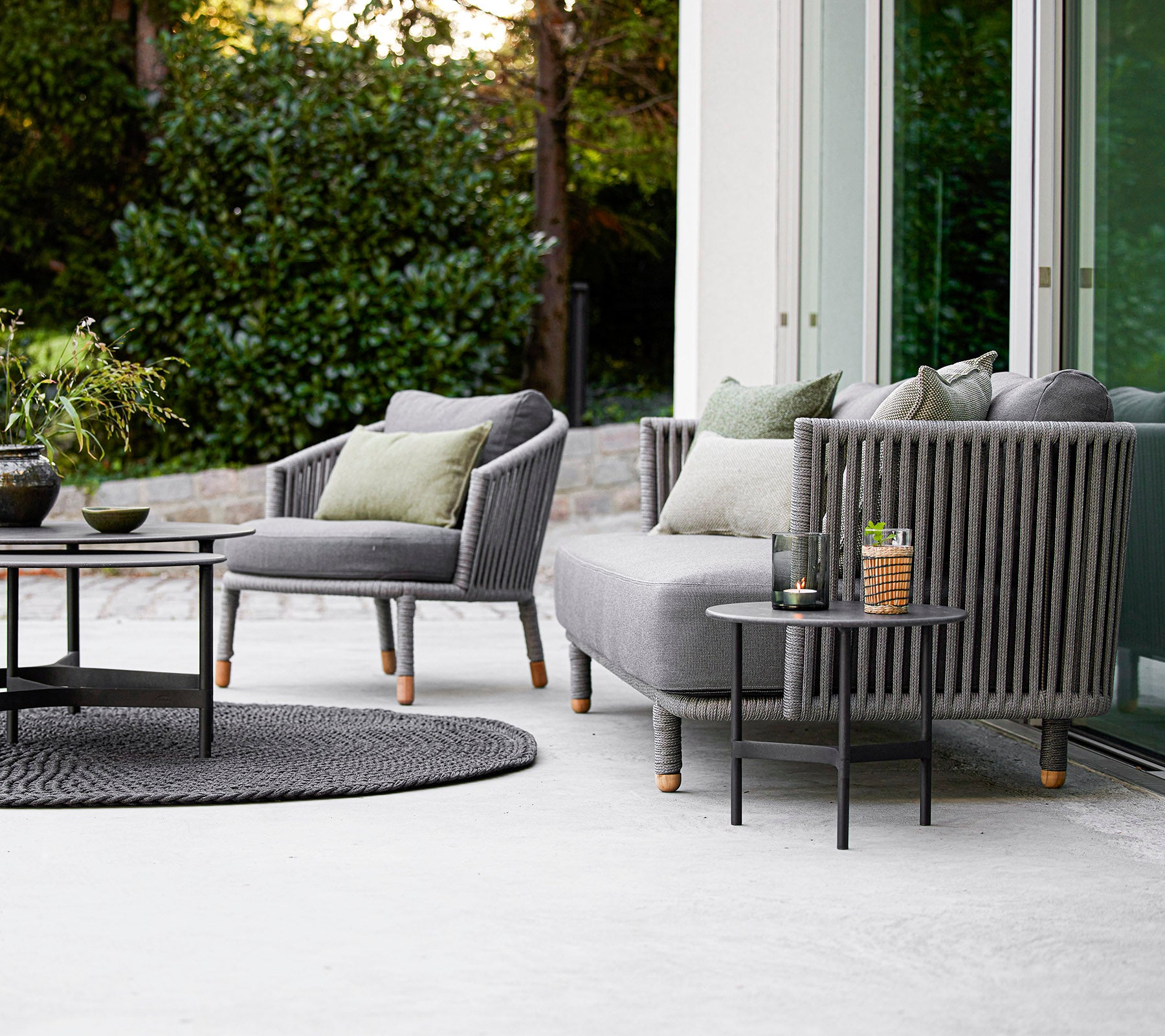 Moderne buitenzitset met een bank en fauteuils met kussens, gecombineerd met een ronde salontafel en decoratieve accessoires.