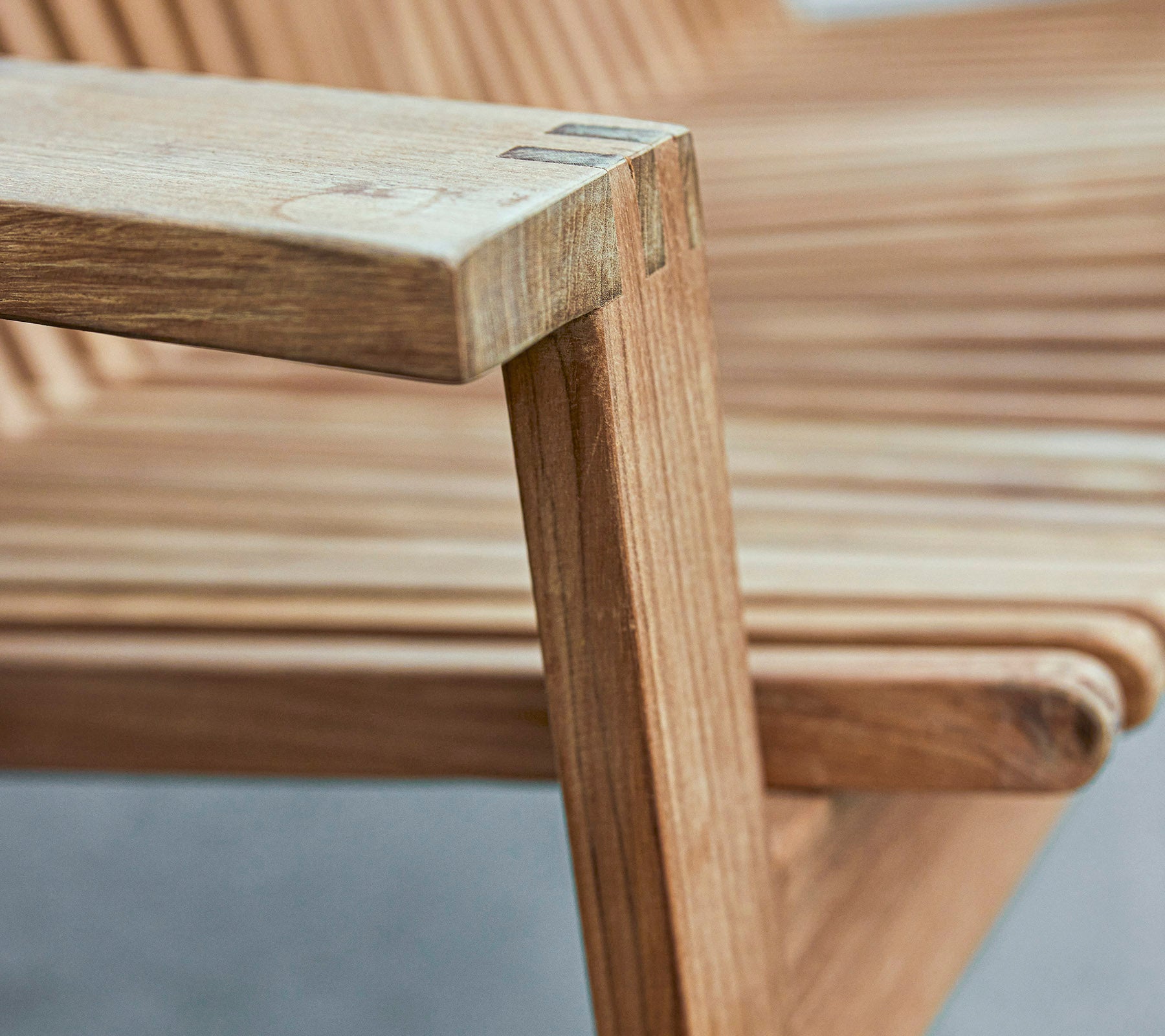 Close-up van een houten stoelarmleuning die een slank ontwerp met lamellenstoel en gladde afwerkingen laat zien.