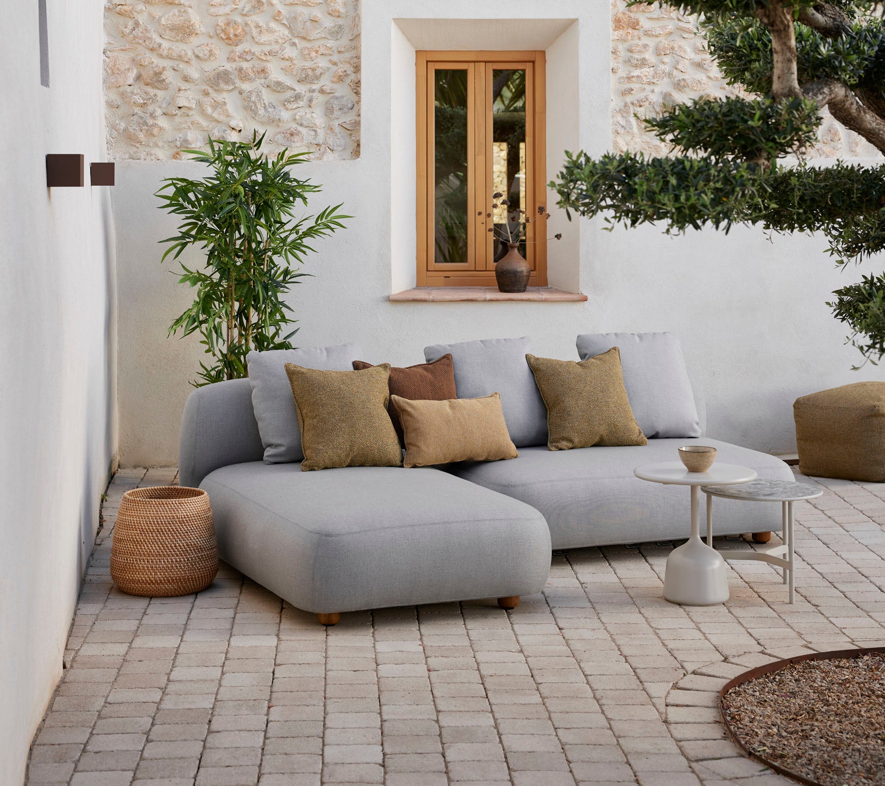 Moderne grijze sectionele sofa met decoratieve kussens, een kleine salontafel en natuurlijke elementen in een gezellige setting.
