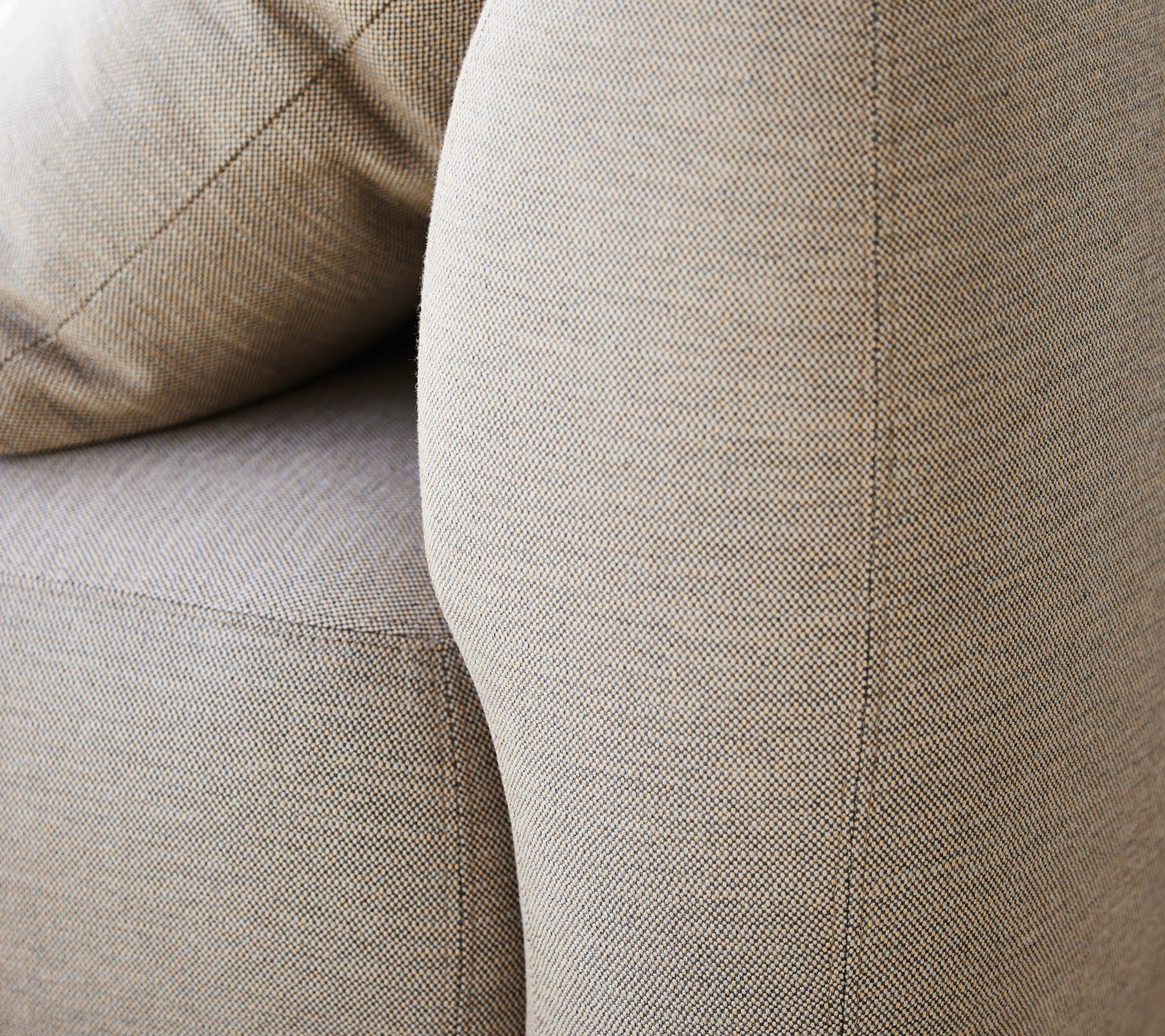 Close-up van een gestructureerde beige bekleding, die de gebogen armleuning en de zachte kussens van een meubelstuk benadrukt.