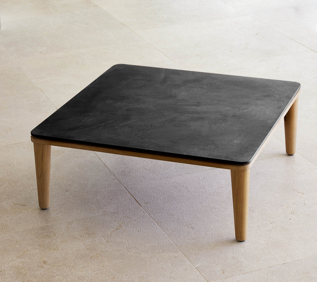 Vierkante zwarte tafel met houten benen in een minimalistische setting.
