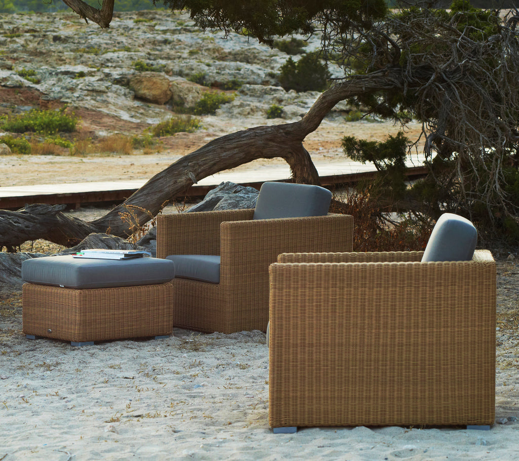 Rattan loungestoelen met grijze kussens in een natuurlijke buitenomgeving.