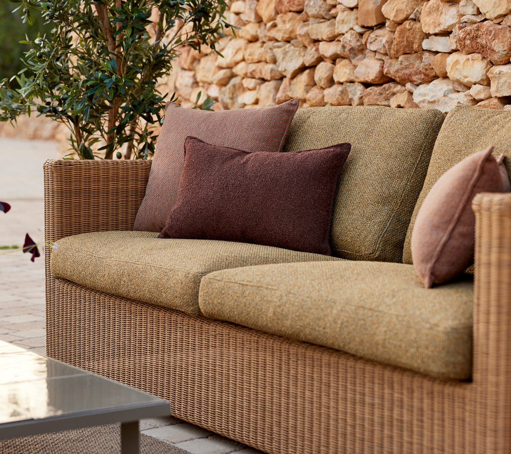 Moderne beige bank met paarse en bruine kussens in een lounge-setting.