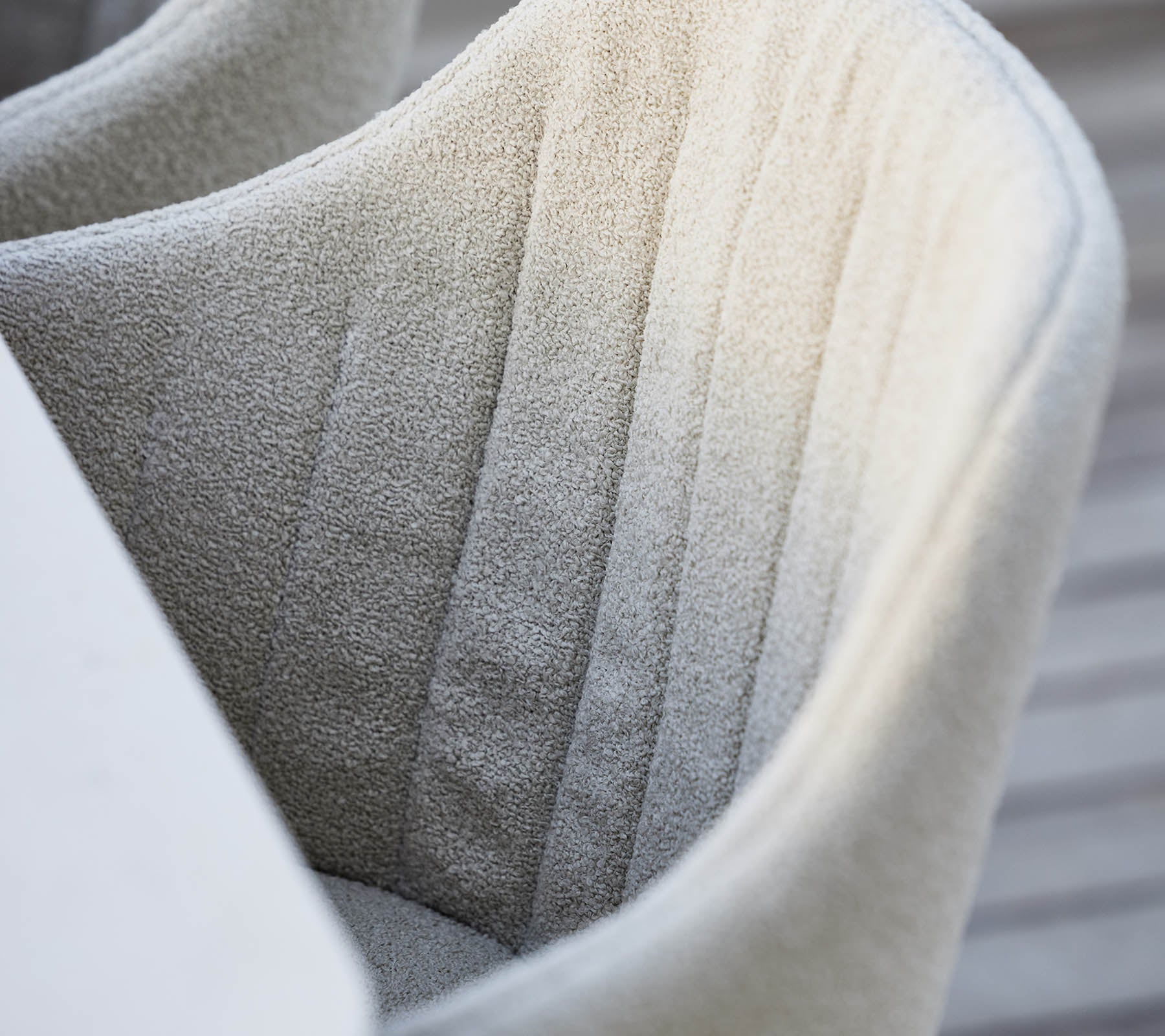 Gestructureerde, volledig beklede stoel met subtiele verticale stiksel, die een zachte, neutrale kleur en een moderne ontwerpesthetiek tentoonstelt.