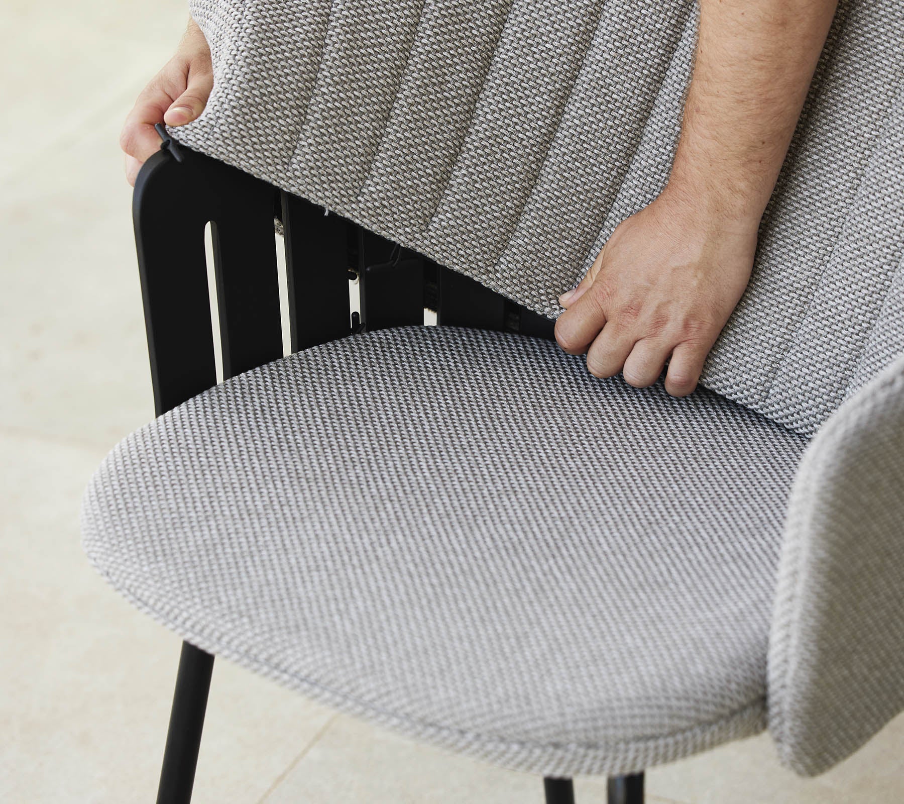 Persoon past de rugleuning van een moderne stoel met een textuurstofzitting aan, die een stijlvol ontwerp en ergonomische ondersteuning toont.