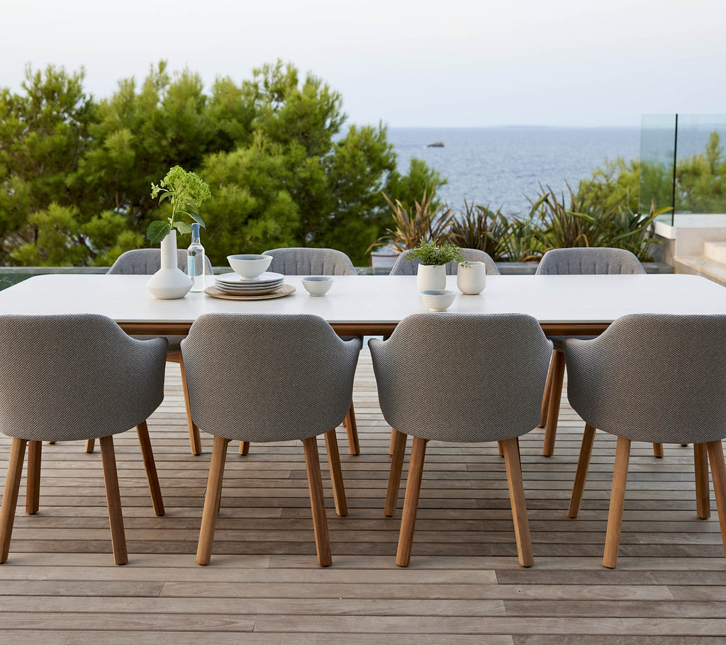 Een moderne tafel met grijs gestoffeerde stoelen, omringd door groen en een serene oceaanzicht, perfect voor dineren en bijeenkomsten.