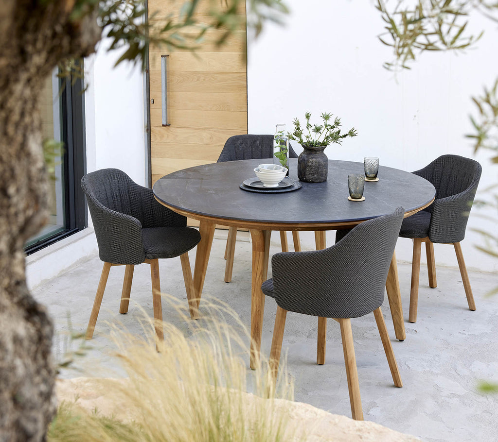 Een ronde tafel omringd door vier stijlvolle stoelen, met een bloemen centerpiece en een eenvoudige tafelsetting.