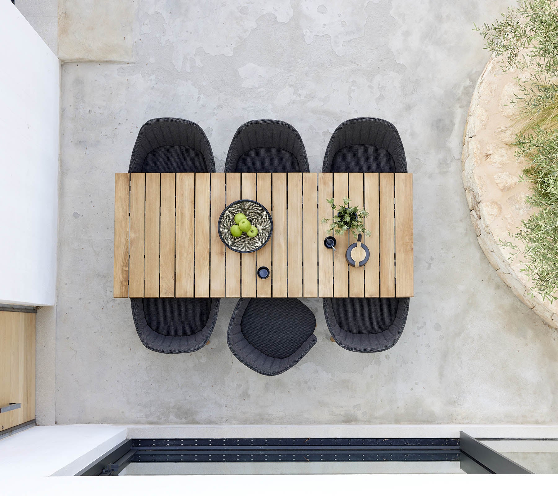 Stijlvolle houten eettafel vergezeld van vier zwarte stoelen, met een schaal met groene fruit en decoratieve planten voor een moderne uitstraling.
