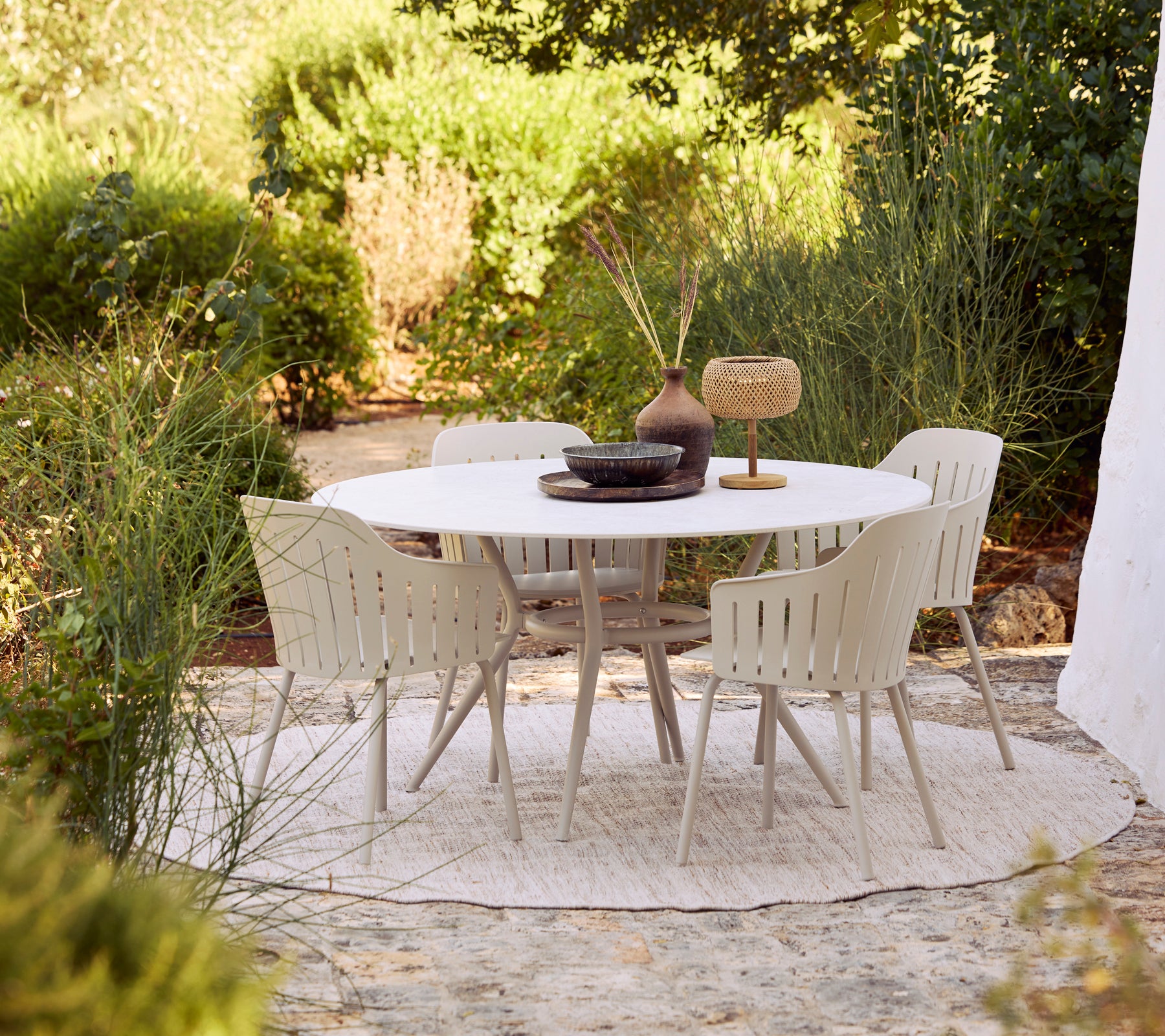 Buiten eetset met een witte ronde tafel en beige stoelen omringd door groen.