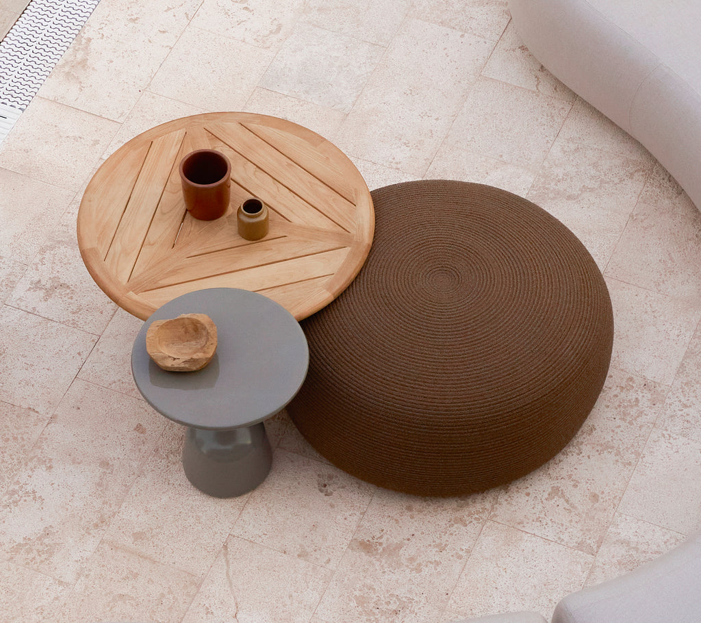 Een grote ronde poef in bruin naast een houten salontafel met een geometrisch design, met kleine decoratieve items bovenop.