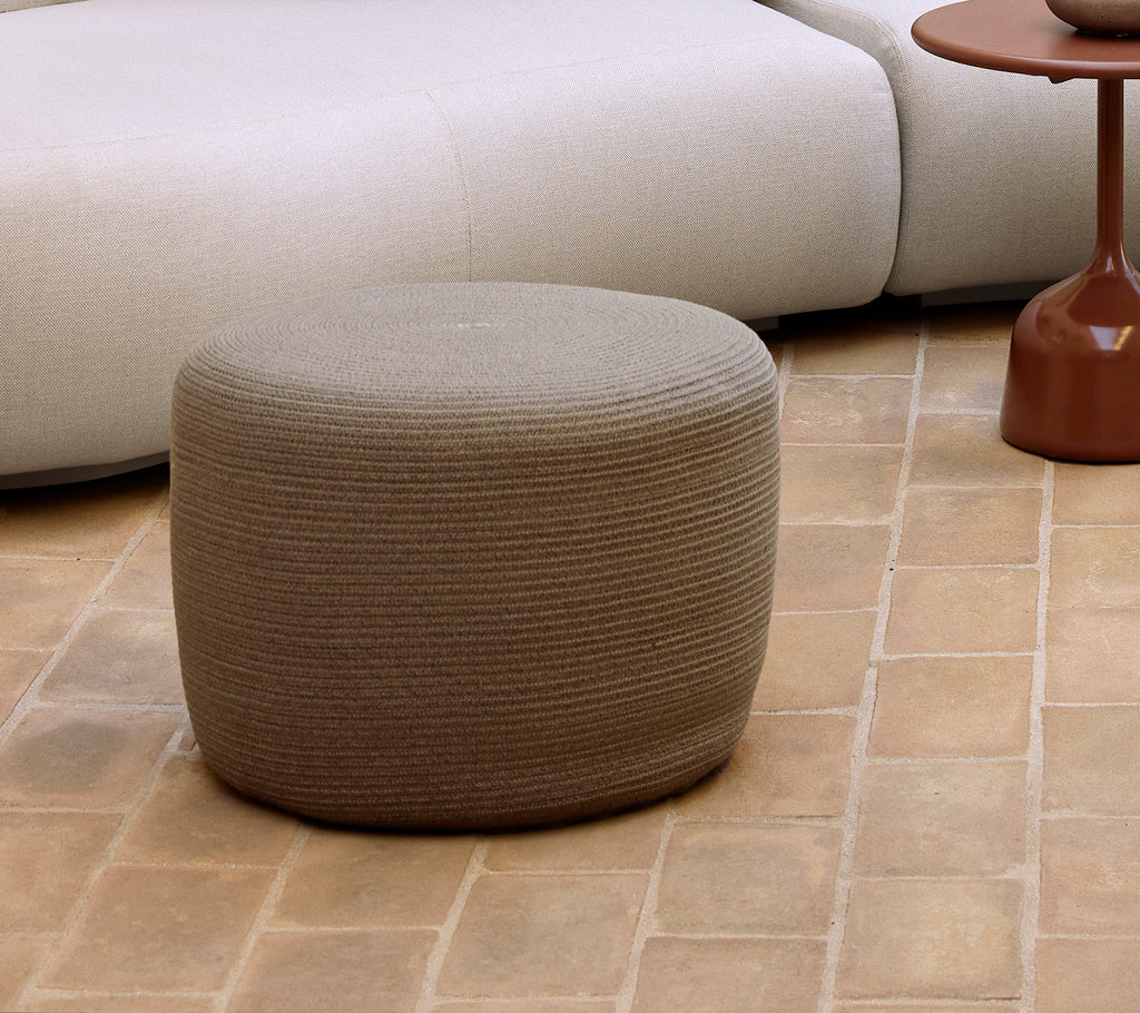 Kleine taupe ronde poef met een gestructureerd oppervlak, die moderne meubels en decoratiestijlen aanvult.