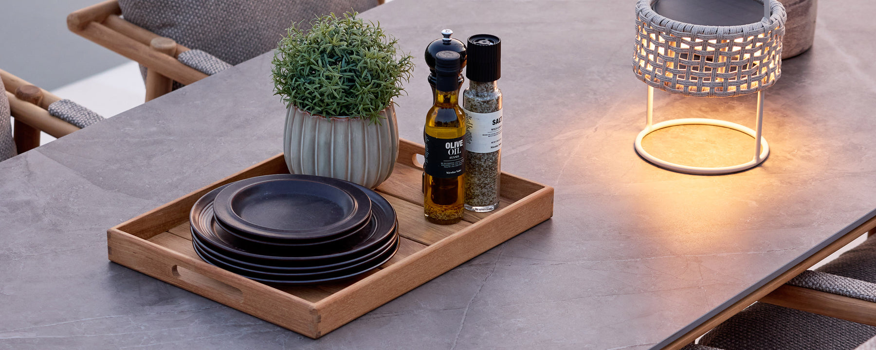 Zwarte borden, fles olijfolie en kleine plant op een dienblad op een eettafel gerangschikt.