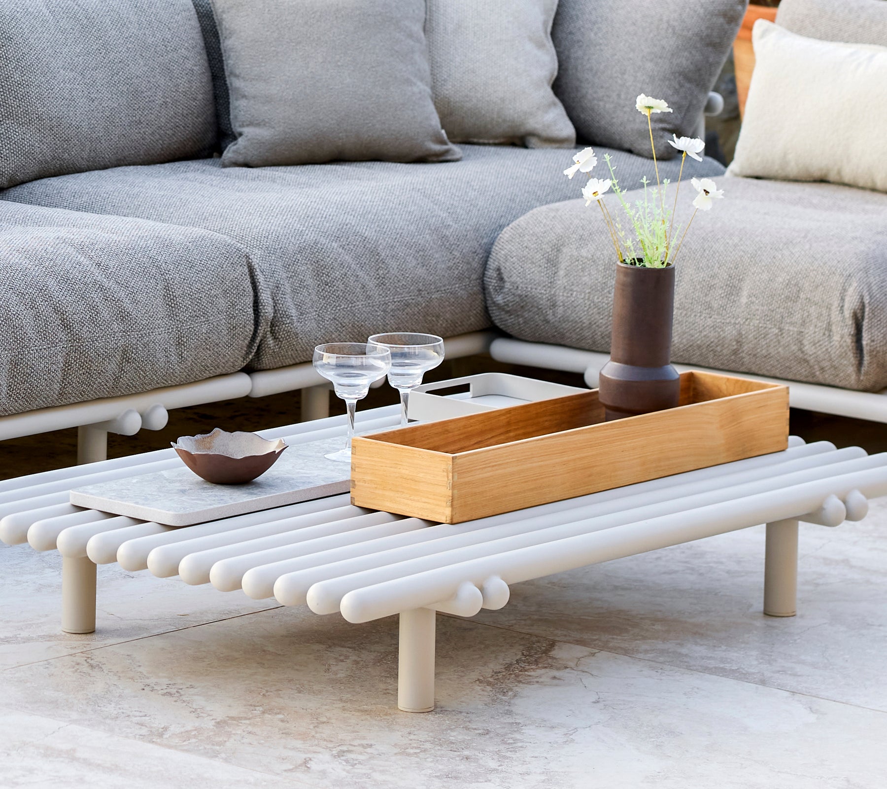 Een stijlvol salontafel met een teak opbergdoos, met een minimalistisch ontwerp en decoratieve elementen zoals glazen en een kleine vaas.