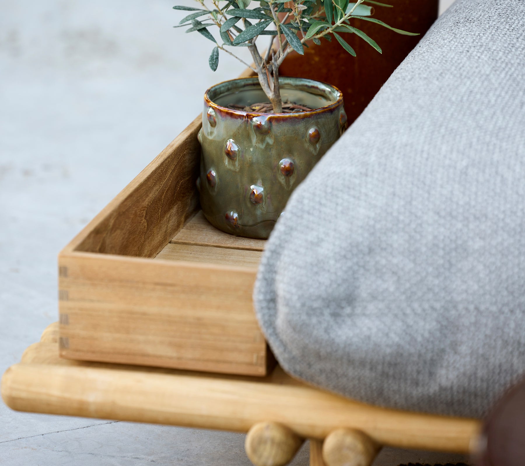 Houten dienblad met grijze kussen en groene pot met een plant.