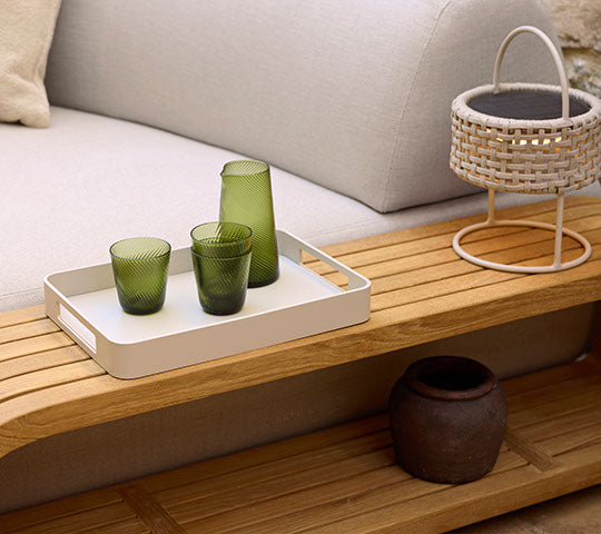 Een houten salontafel met een dienblad met groen glaswerk, een decoratieve mand en een donker keramiekpot.