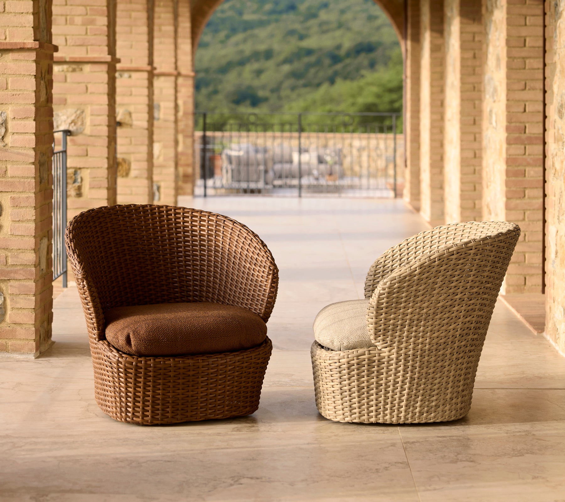 Twee stijlvolle loungestoelen voor op de kust in bruin en crèmekleurig wicker, met comfortabele kussens en een modern design.