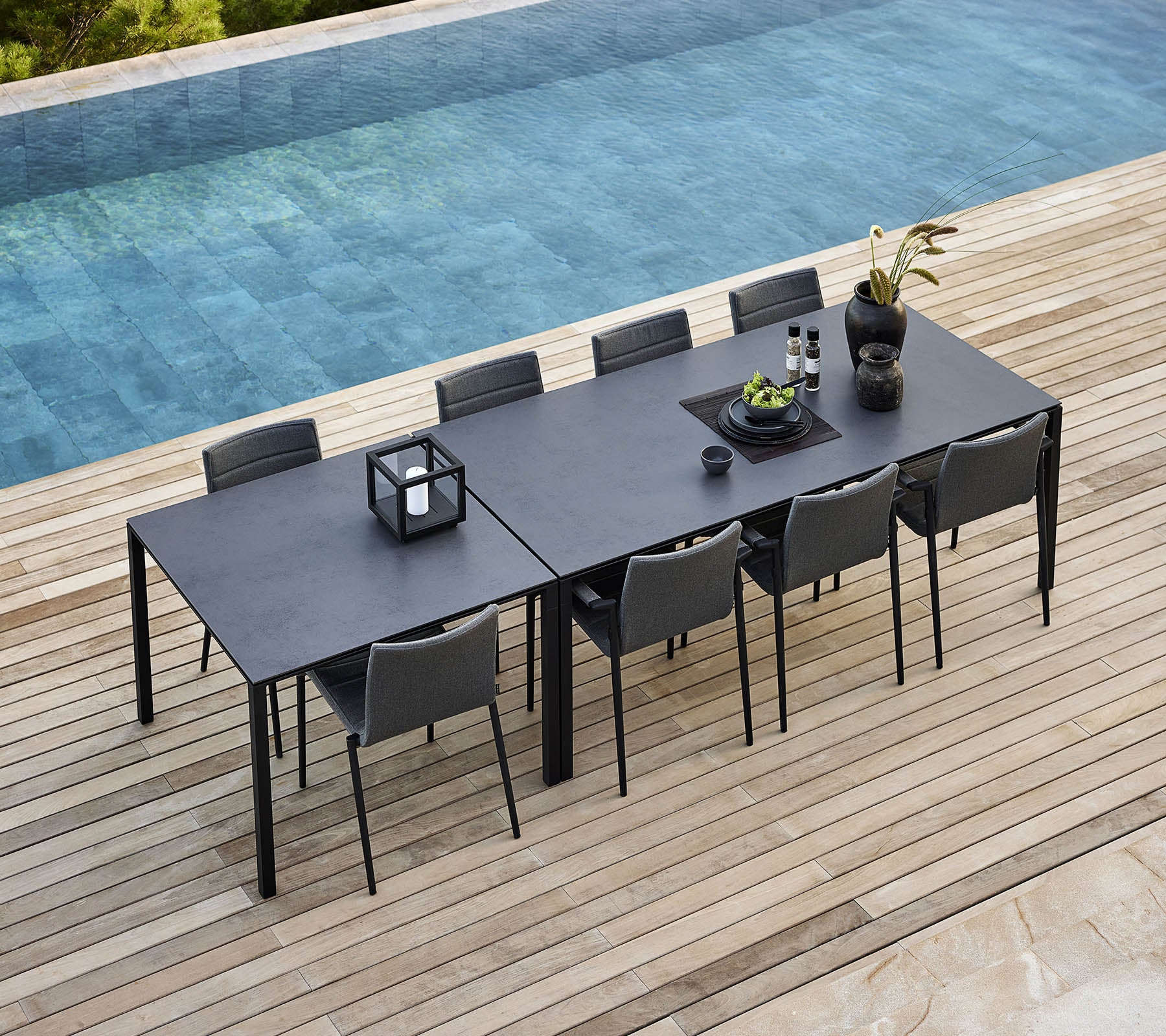 Een strak eettafel met een puur tafel en moderne stoelen, versierd met decoratieve planten en accessoires naast een rustige pool.