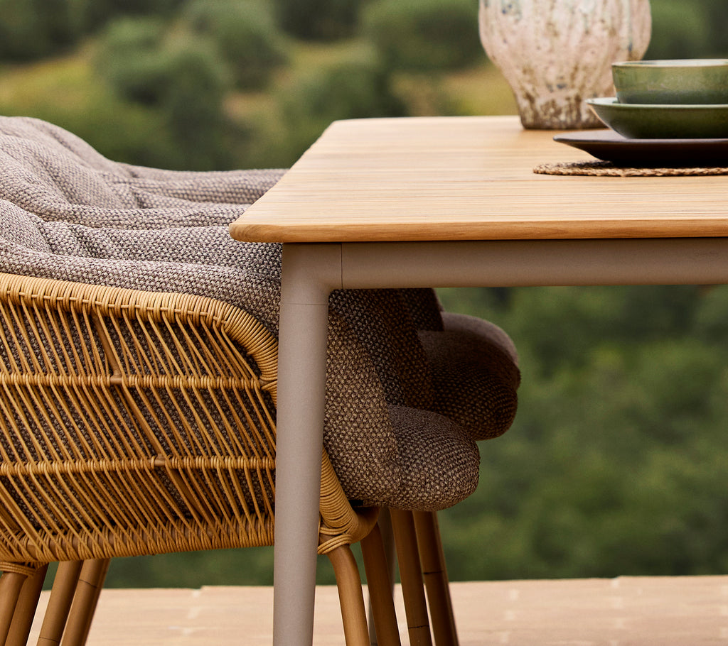 Een close-up van een Core eettafel met een Stay-stoel, voorzien van geweven stof en een groen bord tegen een natuurb backdrop.