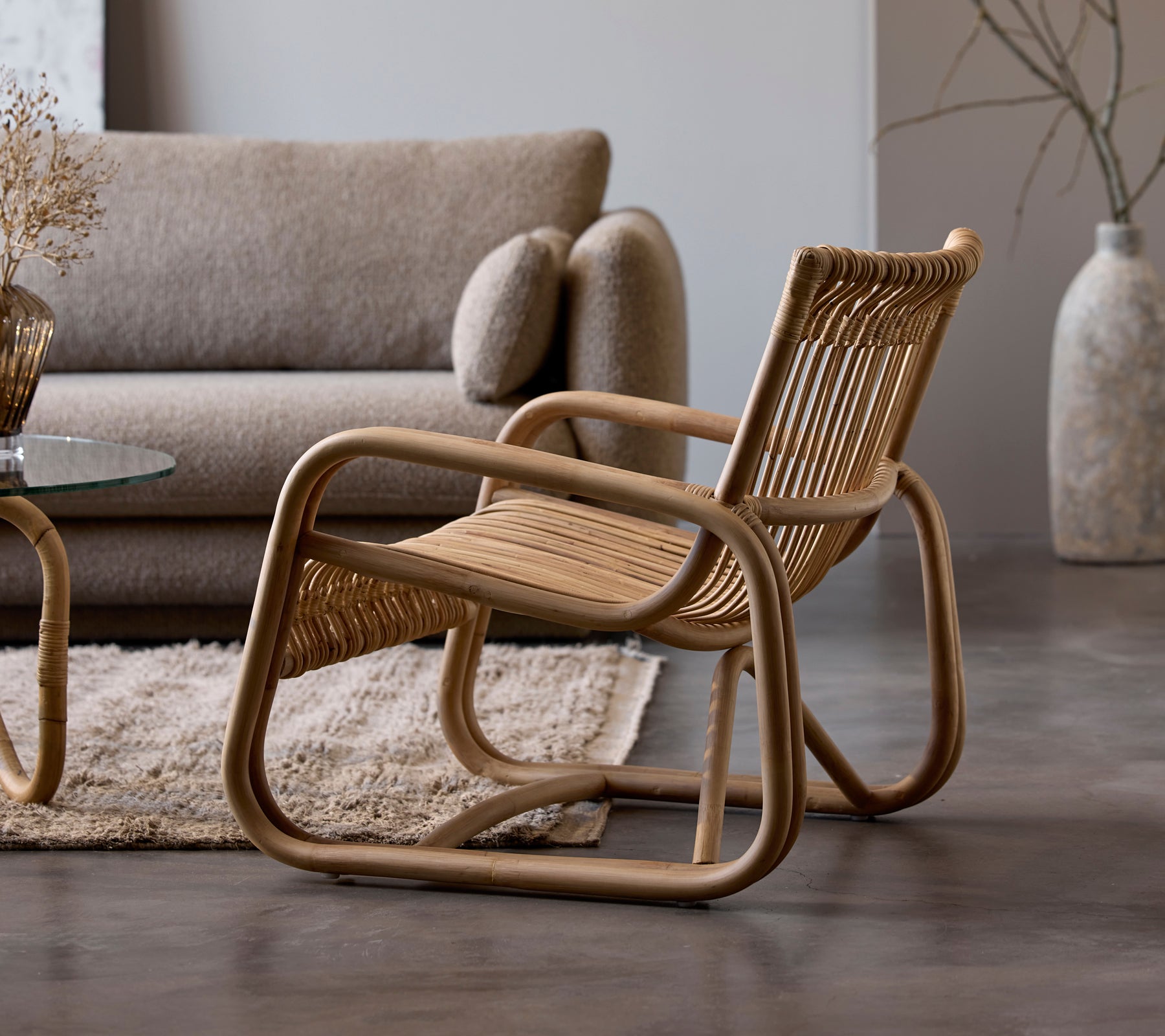 Rattanstoel naast een beige bank en een glazen tafel in een moderne lounge-instelling.