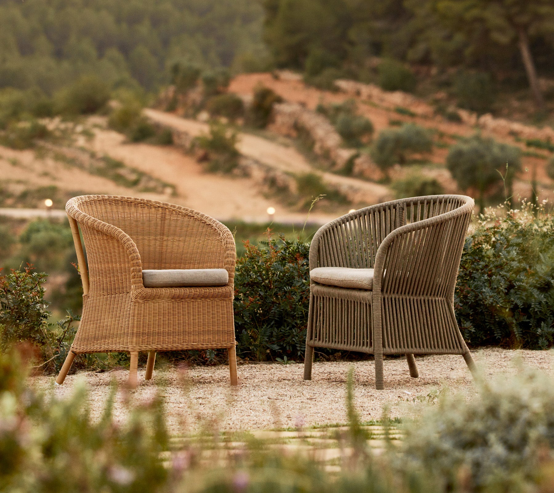 Twee stijlvolle Derby-stoelen in contrasterende kleuren, gezet tussen groen met een schilderachtige achtergrond.