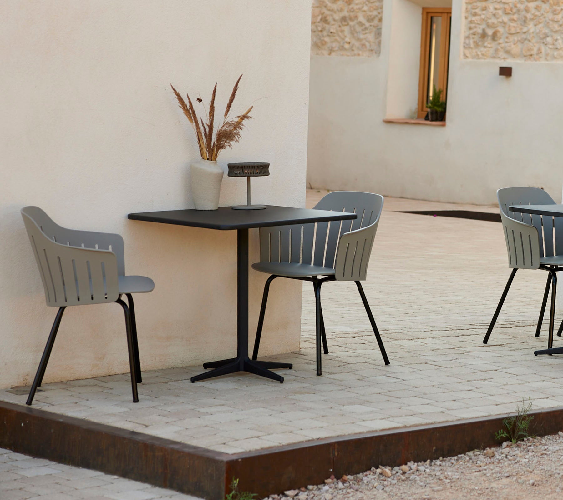 Een moderne café tafel met twee stijlvolle grijze stoelen, vergezeld van een decoratieve vaas, tegen een eenvoudige achtergrond.
