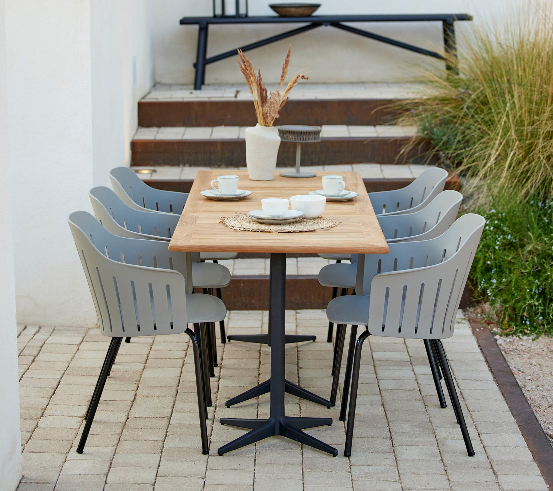 Een stijlvolle eetopstelling met een houten tafel omringd door grijze stoelen, aangevuld met decoratieve items en groen.