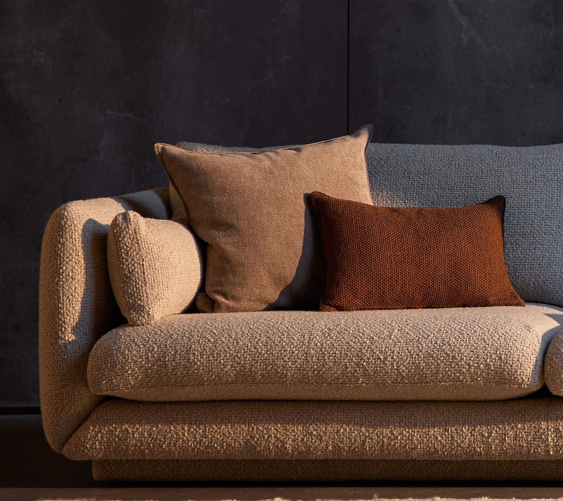 Essence en Rise scatterkussens geplaatst op een gestructureerde Bloom-sofa, met neutrale tinten tegen een donkere achtergrond.