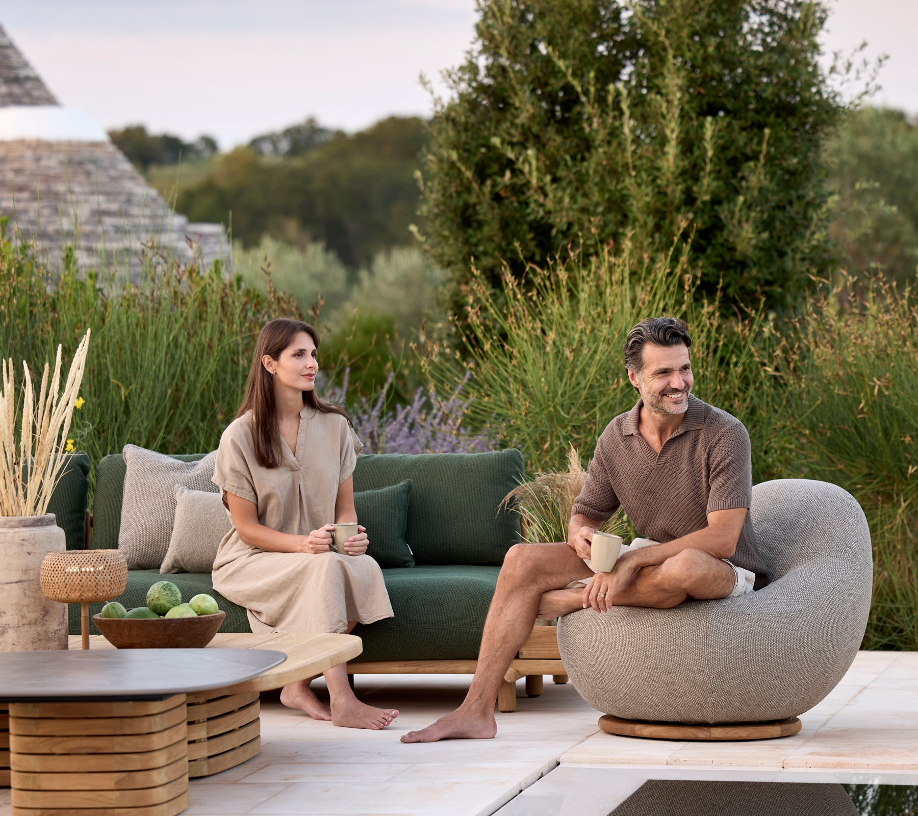 Moderne lounge met groene bank, grijze ronde stoel en bruine tafel omringd door groen.